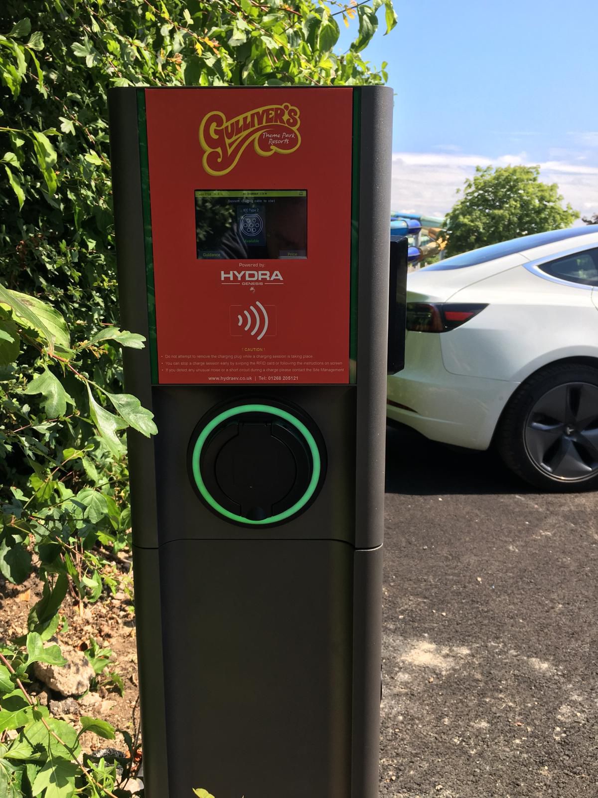 A Hydra Genesis Dual 22kW Socket Only AC EV Charger installed at Gulliver's World theme park. The charger is sleek and modern with two charging sockets back to back. It features a built in contactless terminal for convenient debit and credit card payments, allowing visitors to easily charge their electric vehicles while enjoying the park. The unit is mounted on a purpose built all in one pedestal in a designated EV charging area, surrounded by clear signage indicating it location.